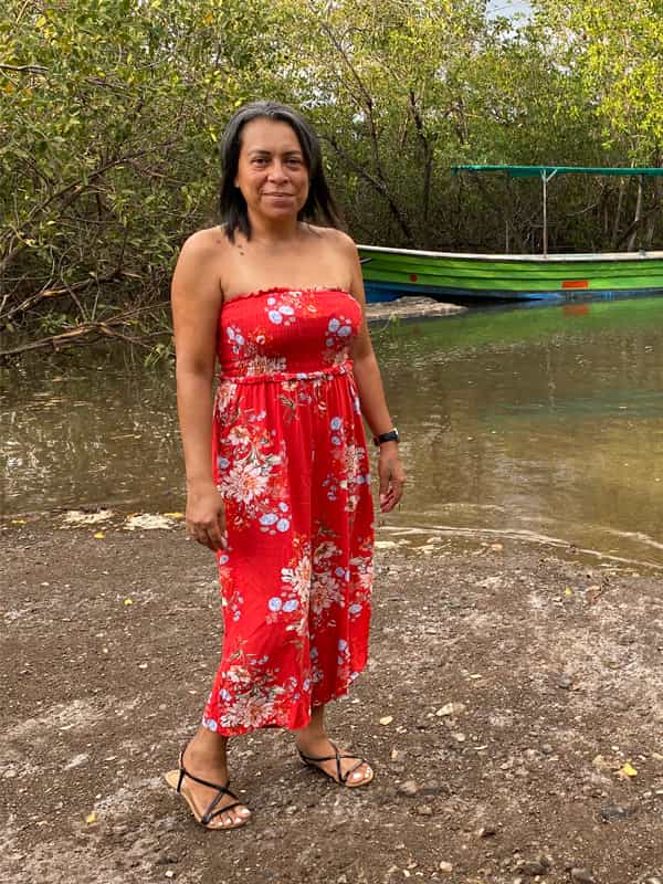 A picture of Karla Carmona standing in from of a little boat in the Pacific coast by Costa Rica Unexplored.