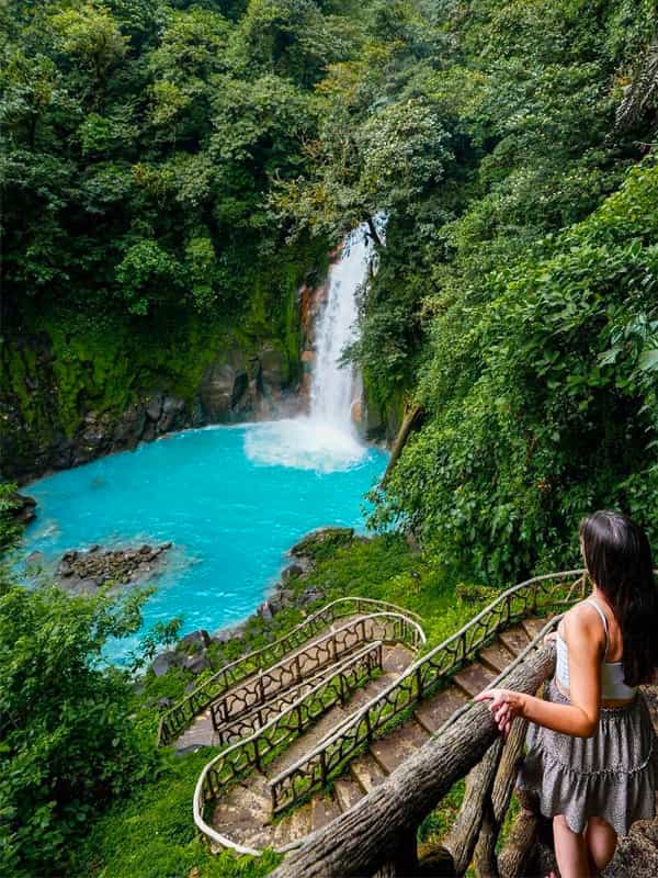 A lady standing while she is admiring the Catarata de Rio Celeste or Light Blue River Waterfall, picture.
