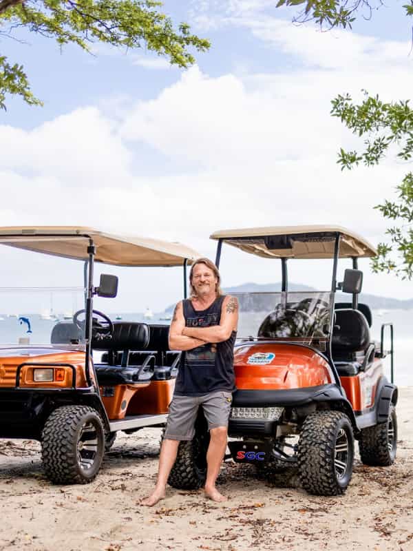 A man standing with two golf carts in from of Tamarindo Beach